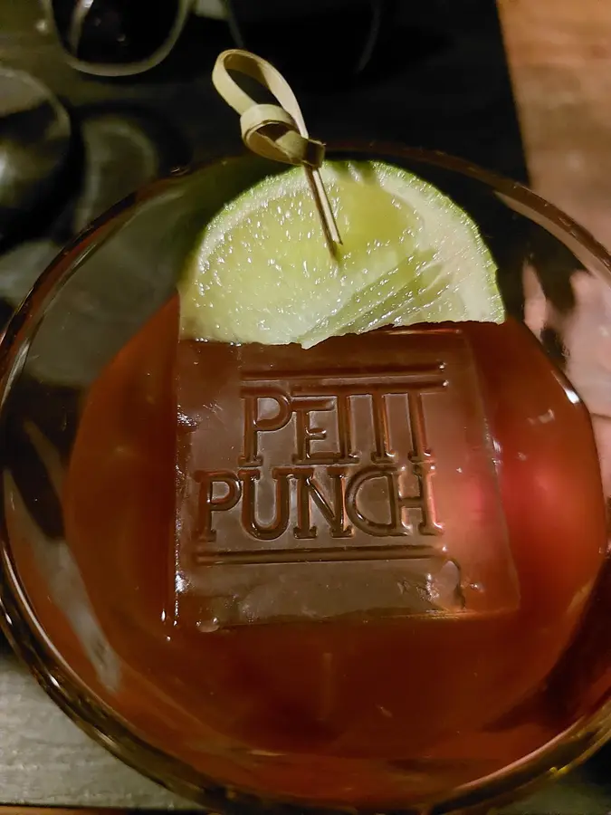 Cocktail mit Limette und einem Eiswürfel, in den der Schriftzug Petit Punch geprägt ist