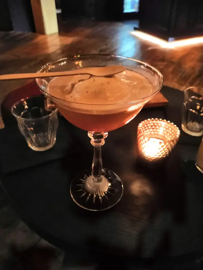 Cocktail in einer Coupette mit Schaum und Holzlöffel, daneben eine Kerze