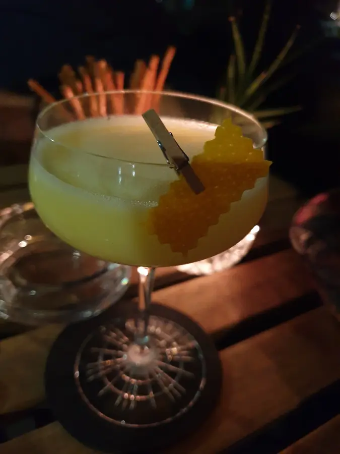 Gelber Cocktail in der Schale mit Orangenzeste an einer Klammer