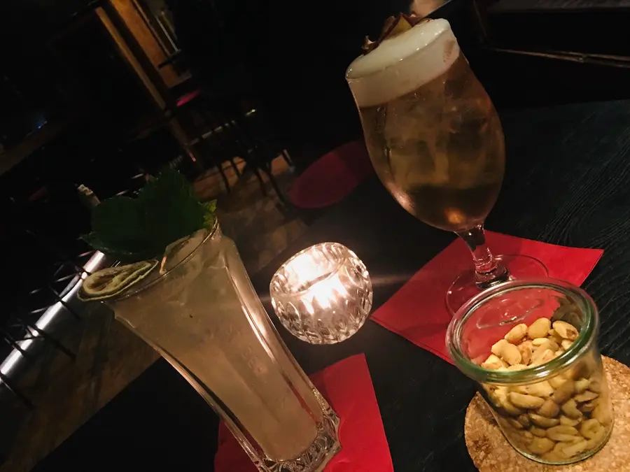 Highball mit Minze, Bier und Erdnüsse auf roten Servietten im Kerzenlicht