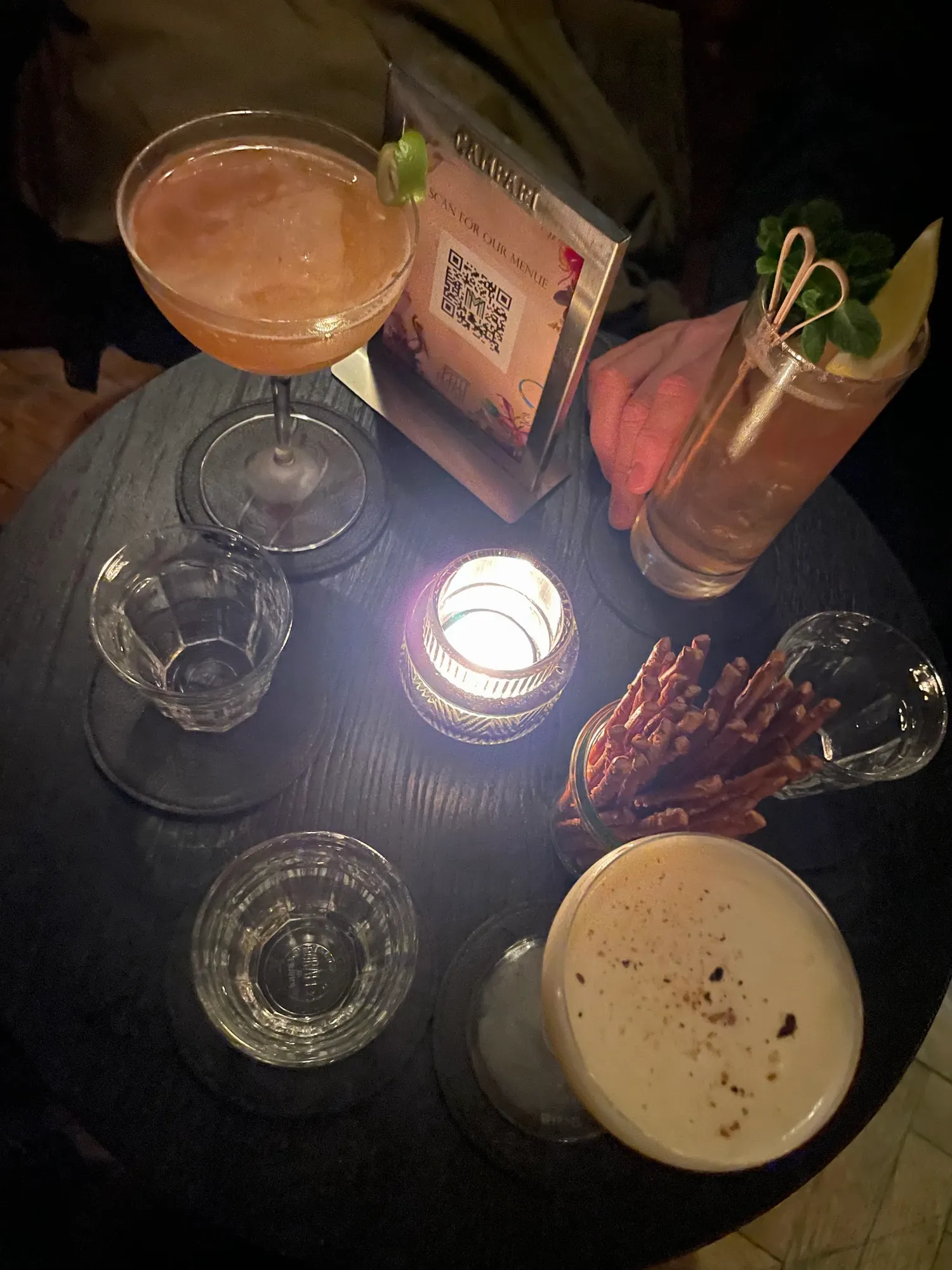 Runder Holztisch von oben mit Kerze, mehreren Cocktails, Wassergläsern und Salzstangen