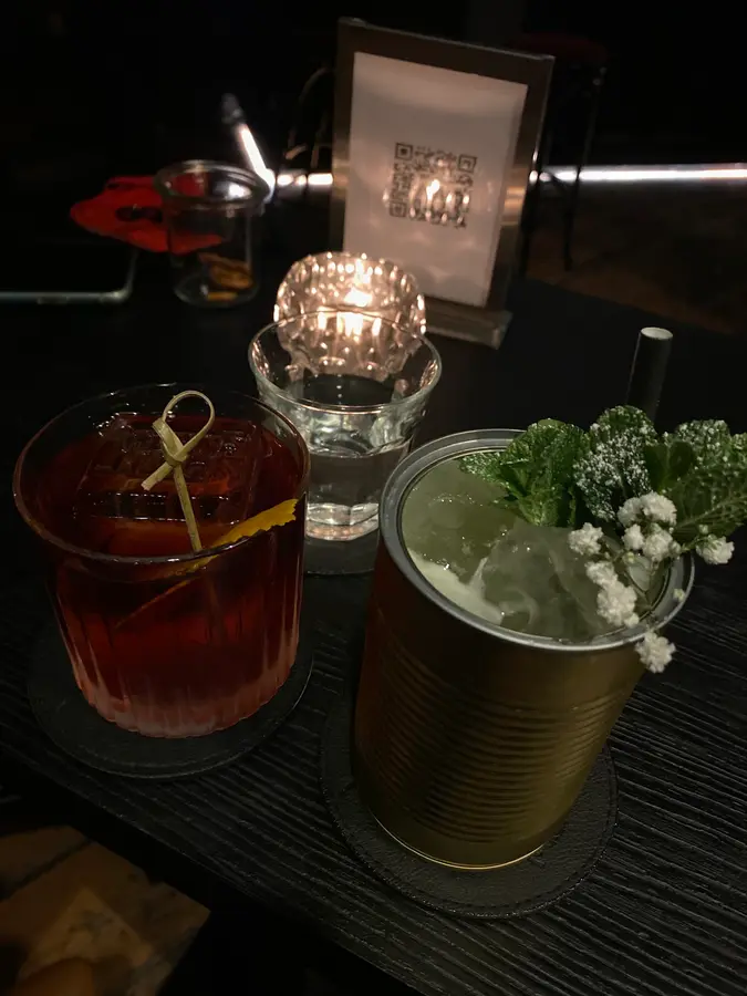 Ein roter Drink im Tumbler und ein Drink in einer goldenen Dose mit Minze und Blüten