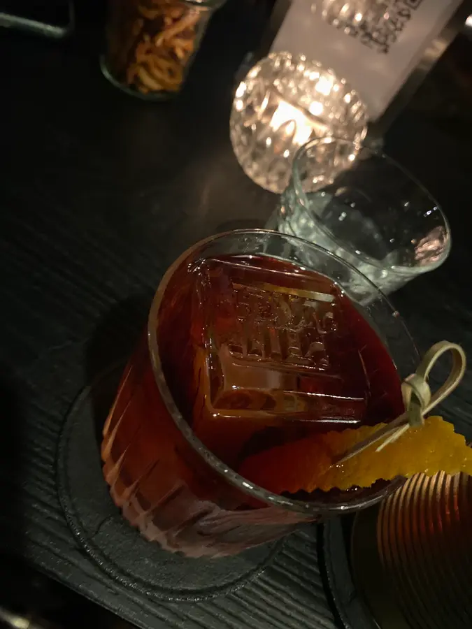 Dunkler Drink im Tumbler mit geprägtem Eiswürfel und Orangenzeste